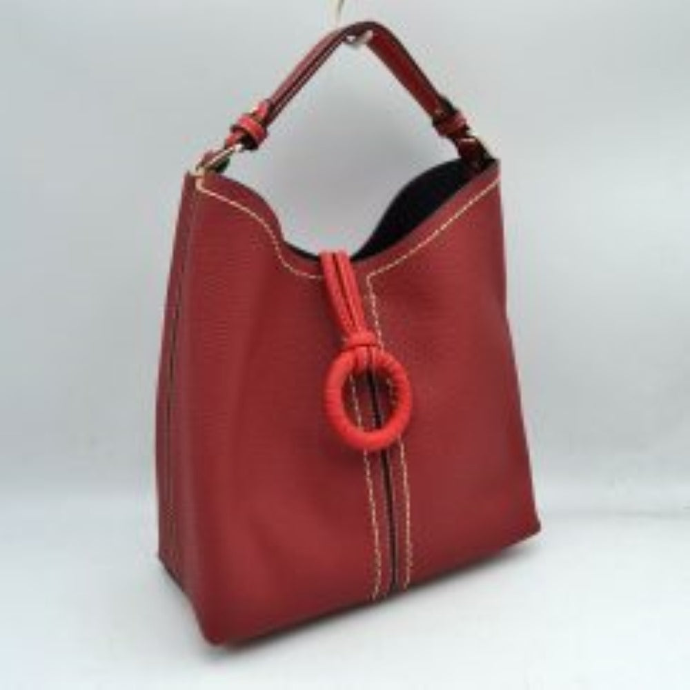 Red This structured everyday bucket bag features a pebbled textured body with a distinctive curved, dip-top opening and prominent contrast stitching details along the front panel. It is designed with a singular flat top handle anchored to the sides by polished metal hardware loops for comfortable carrying. A central loop strap extends from the back to the front