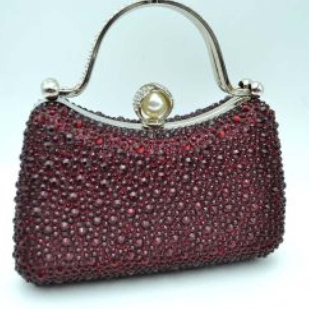 Red This elegant evening clutch bag features a structured silhouette heavily encrusted with shimmering black rhinestones, offering a highly textured and glamorous look for formal events. A sleek, curved metallic top handle lined with delicate crystals rises over the frame for a secure grip, anchored by polished spherical accents. The secure metal frame is highlighted by a prominent decorative clasp featuring a large faux pearl wrapped in rhinestone-studded detailing