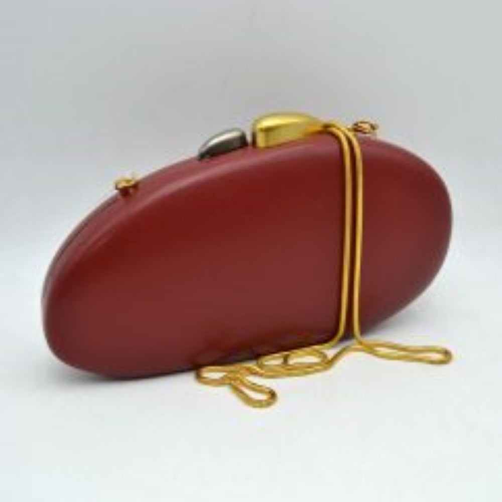 Red This structured hardcase clutch bag features a smooth, rounded oval silhouette designed as a sleek accessory for everyday use. Its single interior storage compartment is secured with a rigid frame closure, accented at the top by a distinctive, asymmetrical two-tone sculptural clasp. A slender, matching metallic snake chain strap connects to small loop anchors on either side via clasp attachments, offering convenient options for hands-free shoulder or crossbody styling.
