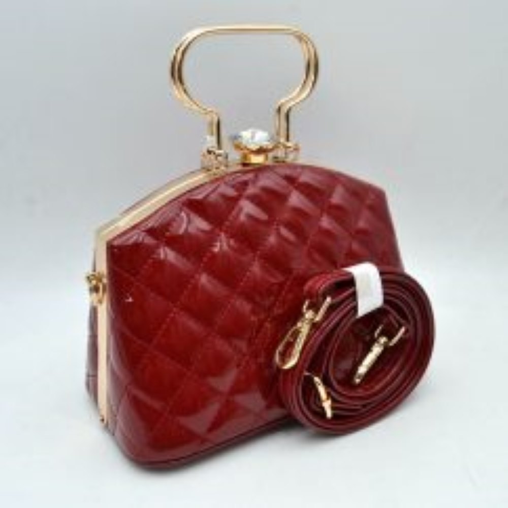 Red This structured handbag features a glossy, quilted exterior pattern that adds texturing to its rigid silhouette for everyday use. It is styled with distinctive metallic top handles and a secure upper storage compartment accessible through a solid frame opening. An ornamental crystal-like clasp sits prominently at the top closure, while side hardware rings accommodate the included matching detachable shoulder strap with metallic clips for multi-way wear.