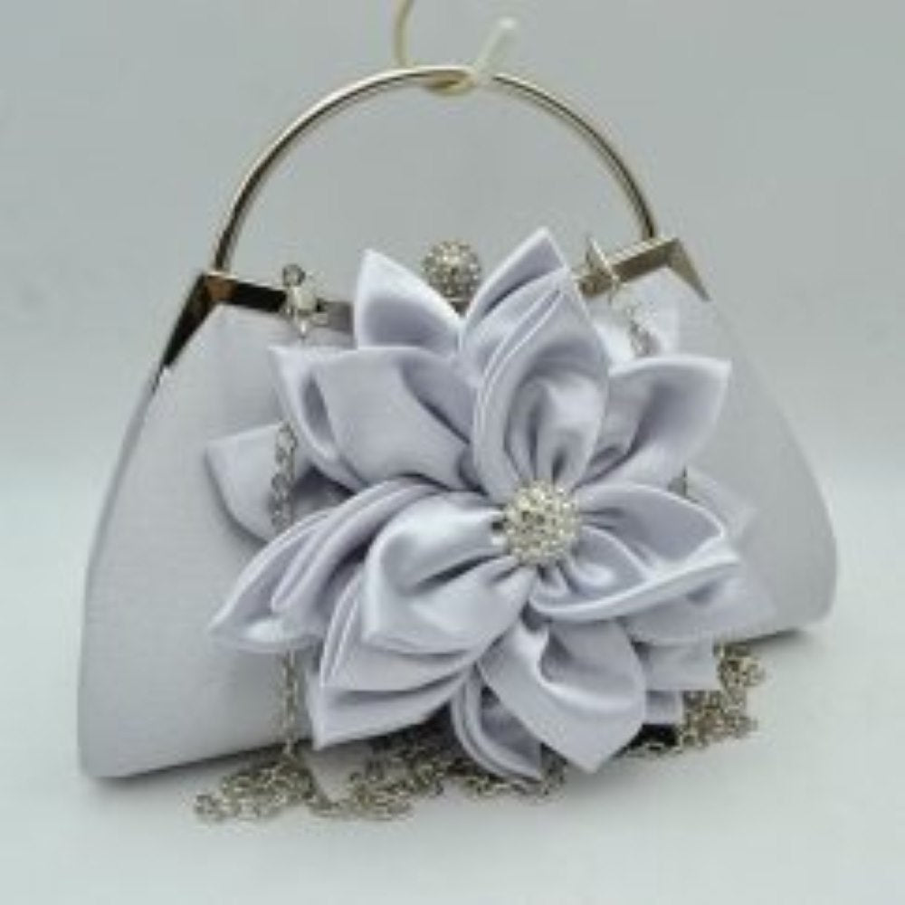 Silver This elegant evening clutch bag features a smooth, structured body dominated by a large, multi-layered fabric flower accent right on the front panel. Designed for special events and everyday formal use, the main storage compartment is secured by a metal frame top with a shimmering, rhinestone-embellished clasp closure.