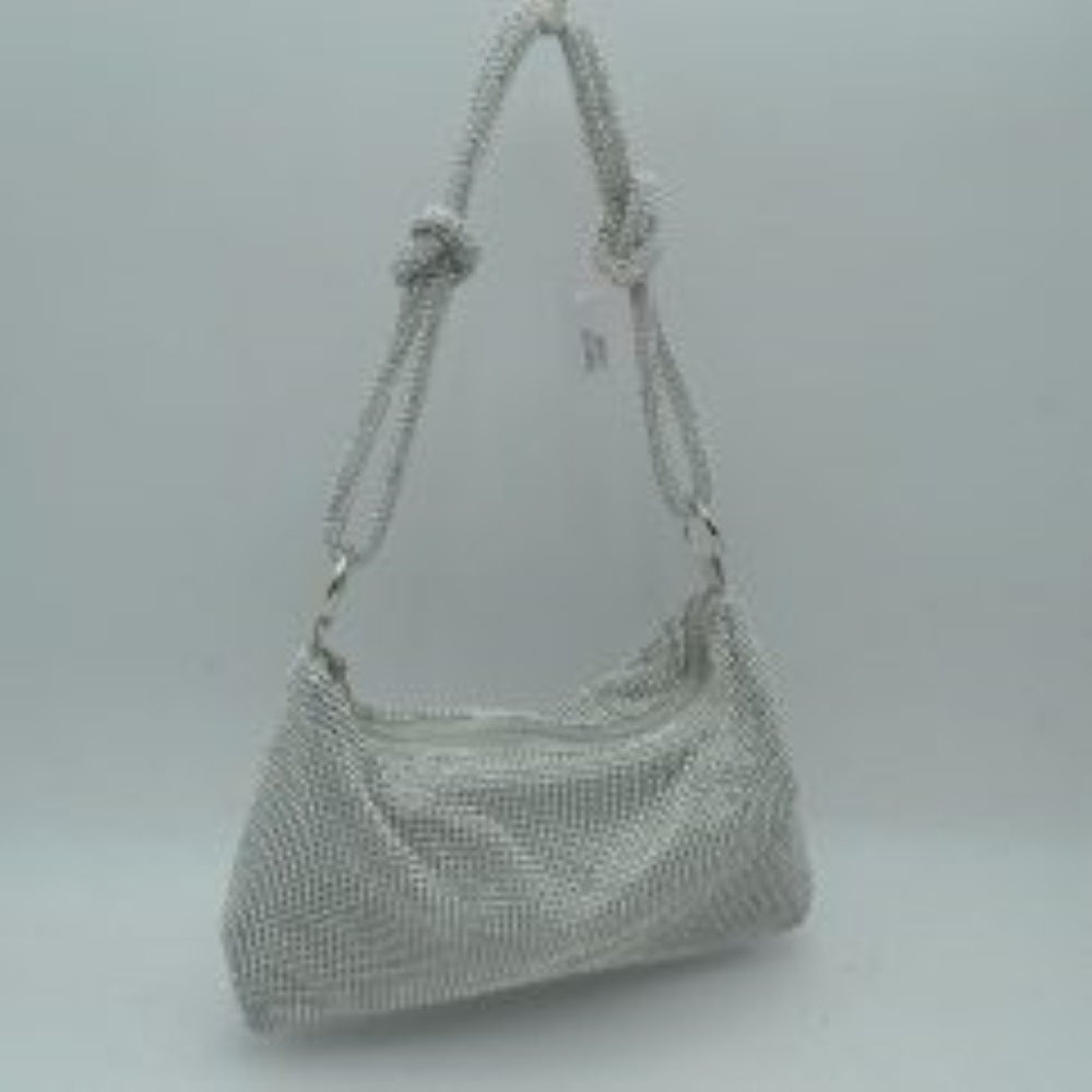 Silver This shoulder bag features a textured grid exterior suitable for versatile everyday use. It includes a main storage compartment accessible via a top zipper closure to keep personal items secure. The bag is completed by a matching textured shoulder strap that features integrated decorative knots on each side and connects to the main body through circular rings.