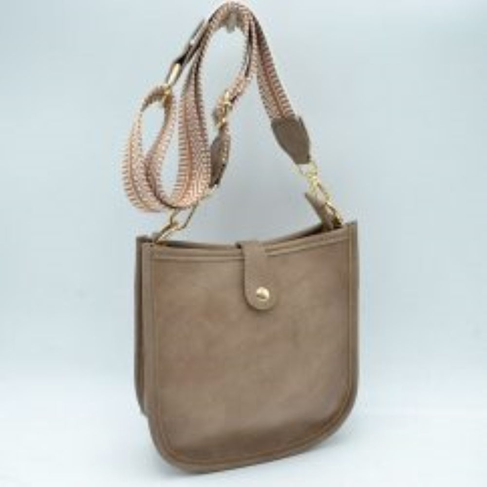 Steel This stylish crossbody bag presents a clean, minimalist design with a smooth exterior finish and a distinct curved, U-shaped silhouette perfect for everyday use. It features an open top main compartment equipped with a small secure tab closure that fastens at the front with a metallic snap button. Adding a striking contrast, the bag is paired with a thick, adjustable fabric strap showcasing a bold geometric pattern