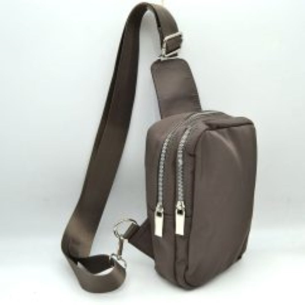 Stone This functional sling bag features a smooth, clean exterior w/ a structured vertical silhouette designed for active everyday use. It offers multiple organized storage compartments, including a primary back section and a secondary front pocket, both accessed via parallel top-curved zipper tracks w/ sleek metallic pulls. The bag is equipped w/ a wide, woven fabric shoulder strap attached to a integrated top panel and secured w/ an adjustable metallic buckle to easily customize the carrying length.