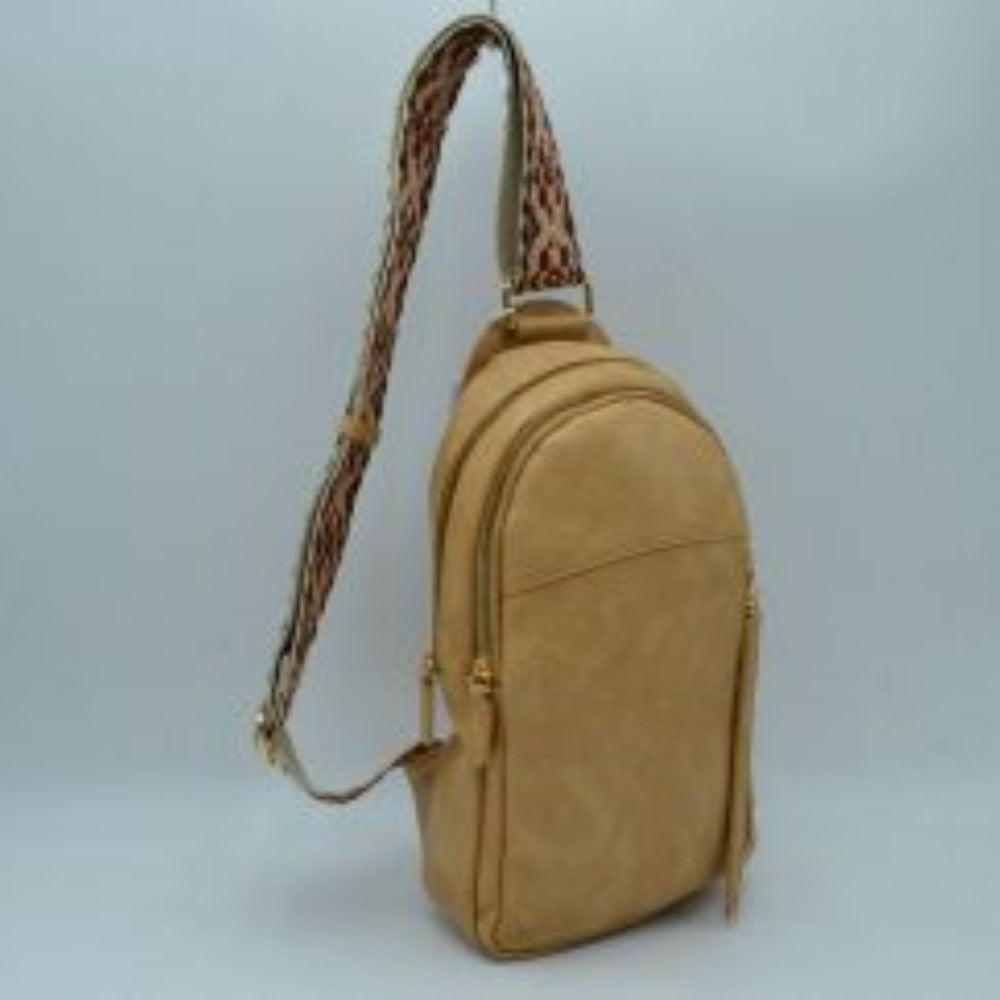 Tan This multi-compartment sling backpack features a smooth texture and a contoured, upright silhouette optimized for daily use. It offers practical storage compartments, consisting of two tiered main sections with independent gold-tone zipper closures alongside a side-access vertical zippered pocket. A distinctive, wide fabric shoulder strap decorated with a detailed geometric woven pattern connects securely to the top and bottom anchors