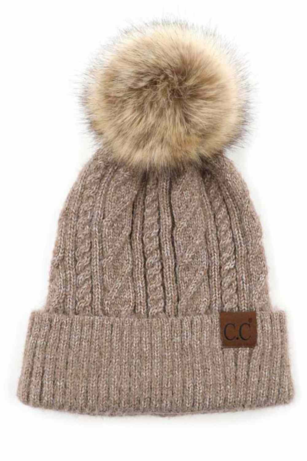 Taupe The C.C Soft Cuff Beanie in Mixed Cable Pattern with Faux Fur Pom features a stylish blend of cable-knit textures topped with a plush faux fur pom for a chic winter look. Made from soft, stretchy fabric with a cozy cuff, it provides warmth, comfort, and a snug fit for cold-weather wear.