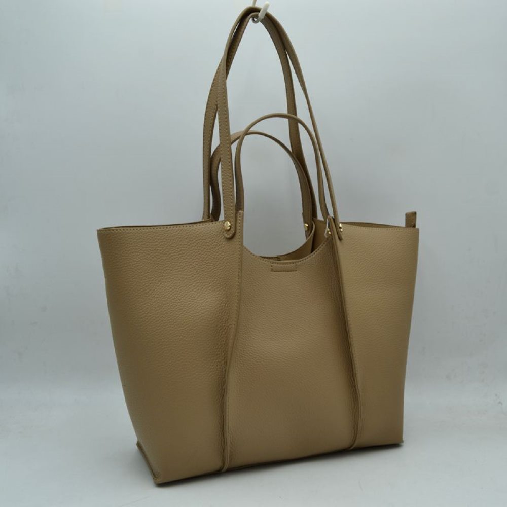Taupe This versatile tote bag is a sophisticated addition to any collection. Crafted from high-quality, durable material, it combines a structured, minimalist shape with a rich, tactile finish. Designed for the modern professional or frequent traveler, it features an elegant central panel design and is adorned with polished gold hardware studs that add a touch of understated luxury.