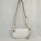 White This versatile everyday bag features a compact pebbled textured body with a slightly curved base silhouette. Designed for organized daily or evening use, the main storage compartment is secured by a top zipper closure and accented with a small decorative metallic turn-lock detail on the side panel. It offers multiple carrying options, equipped with a long, adjustable crossbody shoulder strap and a shorter matching wristlet loop