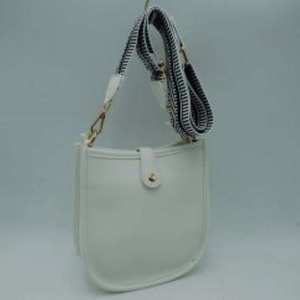 White This stylish crossbody bag presents a clean, minimalist design with a smooth exterior finish and a distinct curved, U-shaped silhouette perfect for everyday use. It features an open top main compartment equipped with a small secure tab closure that fastens at the front with a metallic snap button. Adding a striking contrast, the bag is paired with a thick, adjustable fabric strap showcasing a bold geometric pattern