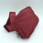 Wine This minimalist bag features a smooth, clean design ideal for versatile everyday use. The main storage compartment is secured by a curved top zipper with dual pulls for easy access to essentials. A wide, adjustable strap extends from the sides, complete with a matching slider to easily customize the fit for comfortable carrying.