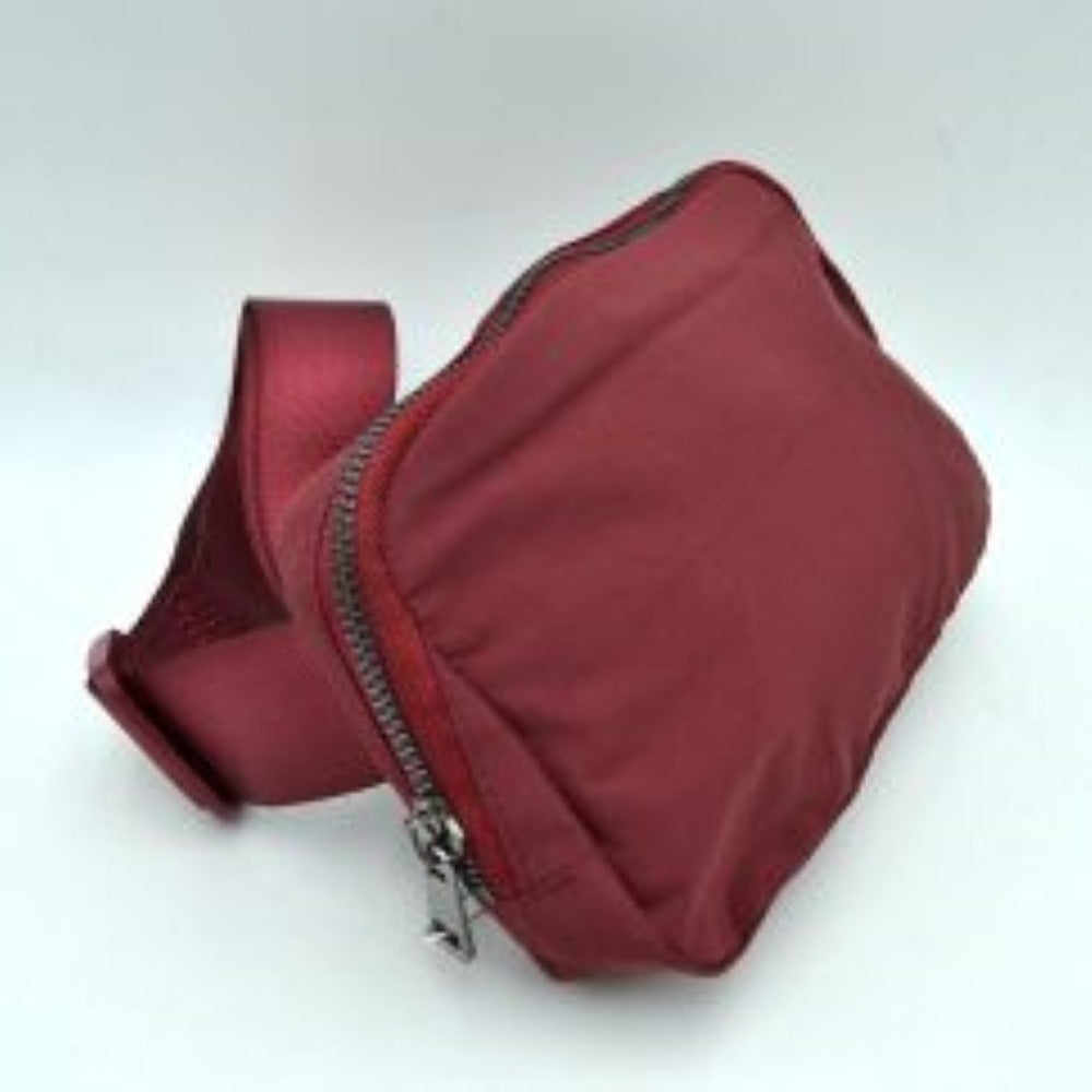 Wine This minimalist bag features a smooth, clean design ideal for versatile everyday use. The main storage compartment is secured by a curved top zipper with dual pulls for easy access to essentials. A wide, adjustable strap extends from the sides, complete with a matching slider to easily customize the fit for comfortable carrying.