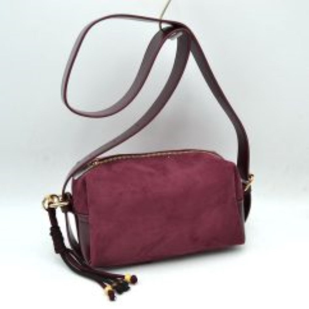 Wine This sleek crossbody bag balances a structured design with a soft matte texture for an understated daily accessory. It features a compact, rectangular body secured by a top-zipper closure that keeps essential items neatly contained. A wide, smooth shoulder strap connects via metallic side loops, allowing for comfortable hands-free carrying. The minimalist look is accented by a decorative knotted cord element attached to the side hardware