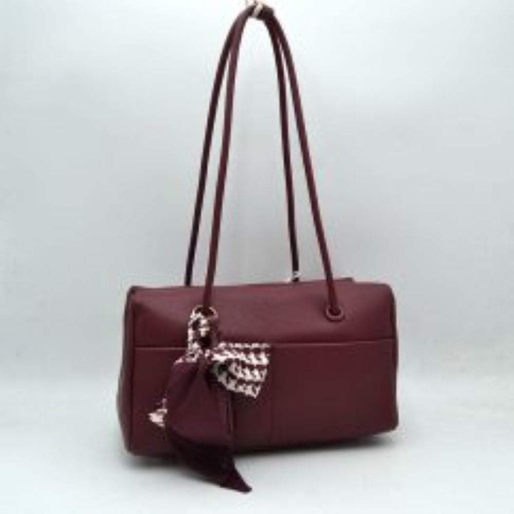 Wine This structural shoulder bag features a textured pebbled exterior in a warm brown tone, offering a contemporary barrel-shaped silhouette for stylish everyday use. Designed with functionality in mind, it features dual long, slim shoulder straps that loop through metallic grommets directly into the body panels. The spacious main compartment opens with a secure top zipper closure, while a matching leather tassel and a patterned houndstooth fabric scarf tied around the front handle base add a playful